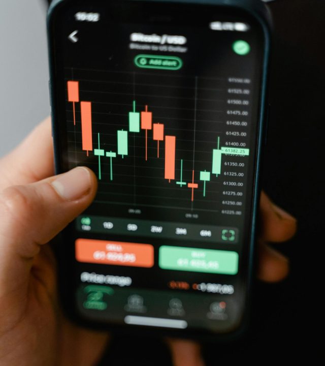 Hand holding smartphone displaying cryptocurrency trading graph in app.